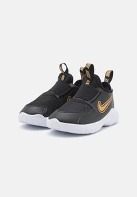 Baskets de sport noires avec une tige en maille, dotées d'une sangle noire sur le dessus, de semelles blanches et d'un logo Swoosh Nike doré.