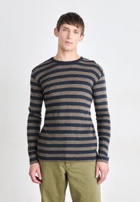 Chemise à manches longues rayée bleu marine et marron clair, col rond, avec une coupe ajustée et une texture lisse. Associée à un pantalon vert olive.