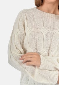 Maglione lavorato a maglia color avorio con un motivo ondulato testurizzato, maniche ampie e vestibilità morbida. Realizzato in un tessuto leggero e morbido.