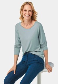 Helles blaues Langarmshirt mit weitem Ausschnitt, kombiniert mit dunkelblauen Skinny Jeans. Glattes Gewebe mit weicher Textur. Keine sichtbaren Muster oder Beschläge.