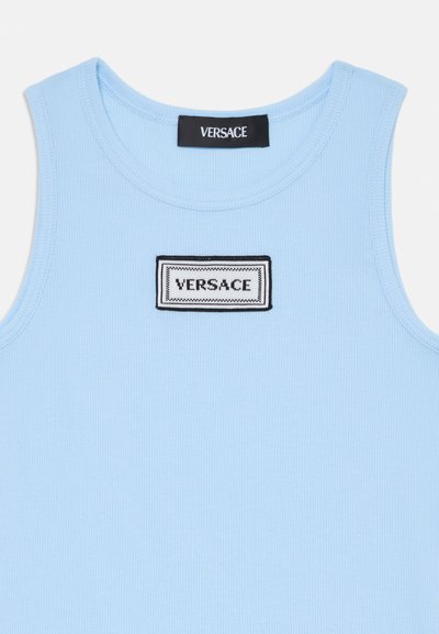 Light blue ribbed tank top with a black and white rectangular Versace logo patch on the front. Smooth texture, round neckline.