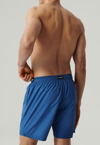 Niebieskie szorty kąpielowe z elastycznym paskiem w talii, bocznymi kieszeniami i jedną kieszenią z tyłu. Wykonane z lekkiego materiału o gładkiej teksturze.