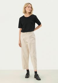 Svart kortärmad t-shirt kombinerad med ljusbeige högmidjade byxor med knäppning fram och sidofickor. Svarta skor fulländar looken.
