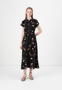 Robe florale noire à manches courtes et boutonnière, présentant des motifs botaniques roses et verts ; tissu léger et coupe longue jusqu'aux chevilles.