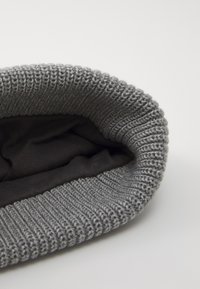 Grå strikket hue med ribbet tekstur og et blødt, mørkt indre for. Designet har en ombukket kant ved skyggen.