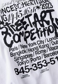 Weißer Stoff mit auffälliger schwarzer Typografie, die Veranstaltungsdetails auflistet: "Street Art Wettbewerb" und verschiedene Städtenamen mit Telefonnummern darunter.
