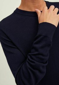 Camicia a maniche lunghe blu navy realizzata in tessuto a maglia ribattuta, con scollo a girocollo e polsini aderenti con una texture liscia.