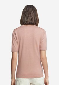 Ljusrosa kortärmad tröja med rund halsringning, slät textur och ribbade muddar. Bakifrån visas en ren och enkel design.