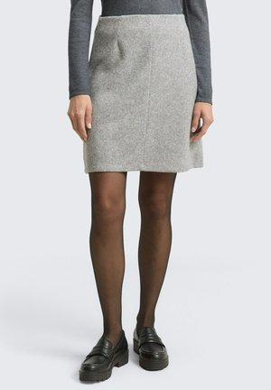 Person wearing a gray knit skirt, black sheer tights, black platform loafers, and a long-sleeve dark gray top, standing against a white background.