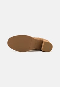 Beżowe zamszowe botki za kostkę z niskim obcasem, teksturowaną podeszwą i gładkim, okrągłym noskiem. Posiadają zamek błyskawiczny z boku, co ułatwia zakładanie.