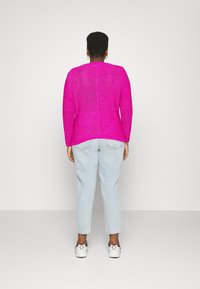 Maglione a maglia fucsia con maniche lunghe e scollo rotondo. Indossato con jeans blu chiaro a vita alta e sneakers bianche. Vista posteriore mostrata.