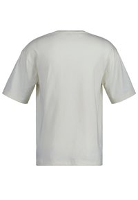 Camiseta de manga corta y cuello redondo en un tono beige claro, con una textura de algodón suave y un corte holgado, sin logotipos ni patrones visibles.
