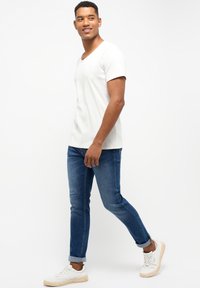 Un tricou alb cu mânecă scurtă și decolteu în V, asortat cu blugi albaștri slim-fit, cu manșete răsucite, și adidași albi cu o suprafață texturată.