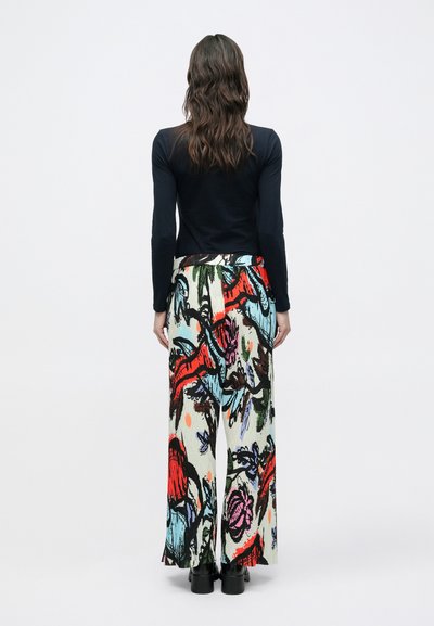 Μαύρο μακρυμάνικο τοπ με εφαρμοστή σχεδίαση συνδυασμένο με μια ροή, πολύχρωμη πλισέ φούστα με floral μοτίβα και έντονες κόκκινες λεπτομέρειες.