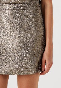 Metalen zilveren minirok met een gestructureerd, geometrisch patroon. Heeft een nauwsluitend ontwerp en een rechte zoom, gedragen op de taille.