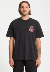 Czarny bawełniany t-shirt z czerwonym i szarym wzorem graficznym na lewej piersi, z krótkimi rękawami i luźnym krojem.