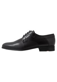 Chaussure habillée en cuir noir avec un dessus lisse et perforé, un bout arrondi et un petit talon. Équipée de lacets et de subtils accents contrastants.