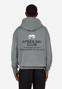 Pelēks pārspīlēts kapuci, kas piedāvā kapuci, ribotas aproces un aizmugures grafiku ar tekstu: "APRÈS-SKI KLUBS", ar kalnu brilles dizainu un citātiem.