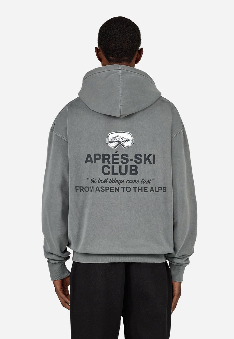 Pelēks pārspīlēts kapuci, kas piedāvā kapuci, ribotas aproces un aizmugures grafiku ar tekstu: "APRÈS-SKI KLUBS", ar kalnu brilles dizainu un citātiem.