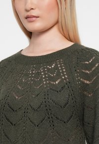 Olive green, dzianinowy sweter z okrągłym dekoltem i teksturowanym, otwartym wzorem z kształtami chevron oraz miękkim wykończeniem.