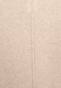 Beige gebreid stof met een zachte textuur en een centrale naaddetail die verticaal loopt. Het materiaal lijkt lichtgewicht en knus.