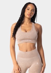 Gaiši brūns sporta komplekts, kas ietver pieguļošu īsās piedurknes topu un augsto jostasvietu leggins, abi izgatavoti no mīksta, strukturēta auduma ar vieglu zīmola identifikāciju.