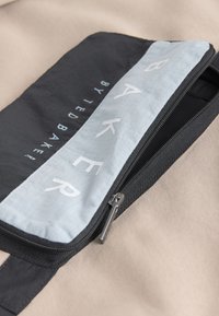 Gros plan sur une trousse zippée noire et gris clair avec « BAKER BY TED BAKER » imprimé sur le tissu.