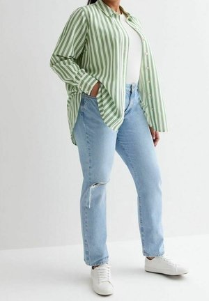 Person wearing light blue distressed jeans, white sneakers, white ribbed top, and oversized green and white striped button-up shirt.