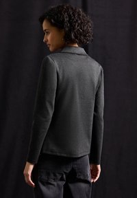 Ciemnoszary żakiet o subtelnej strukturze, z wyciętym kołnierzem i długimi rękawami, noszony na czarnych spodniach.