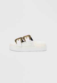 White platform sandals featuring two black straps with ornate gold buckles, textured sole, and smooth finish.