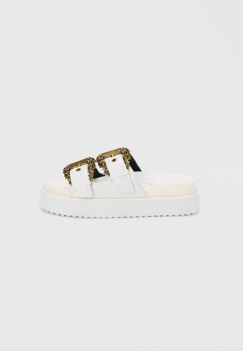 White platform sandals featuring two black straps with ornate gold buckles, textured sole, and smooth finish.