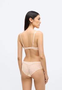 Barackszínű fehérnemű szett áttetsző melltartóval, vékony pántokkal és hozzá illő, geometriai csipkével díszített hátsó paneles alsóval.