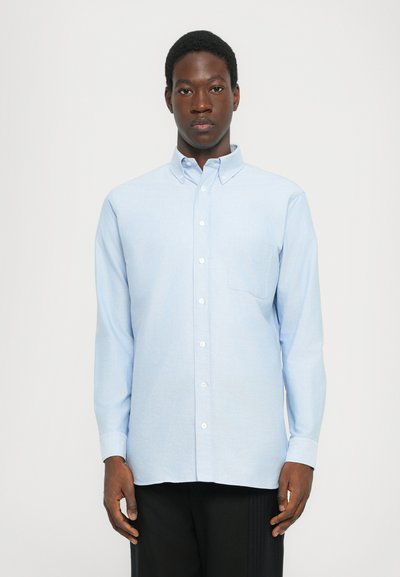 Camicia blu chiaro con maniche lunghe, colletto standard e taschino singolo sul petto. Realizzata in un tessuto testurizzato.