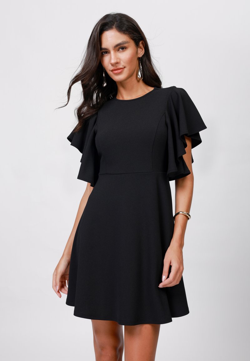Robe noire avec des manches courtes et volantes, corsage ajusté et jupe évasée. Fabriquée dans un tissu lisse, avec un décolleté rond et sans motifs.