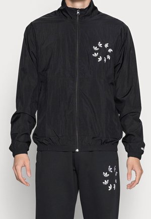Zwarte lichtgewicht jas met een opstaande kraag, rits aan de voorkant en witte logo-details. Gepaard met bijpassende broek met logo-accenten.