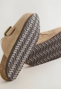 Chaussures en daim beige avec une forme arrondie, dotées de semelles en caoutchouc texturé avec un motif en zigzag et d'un petit accent de boucle.
