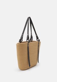 Beige vævet tote taske med lange sorte dobbelte remme med hvid syning, vist vinkelret mod en helt hvid baggrund.