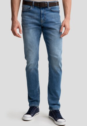 Jeans in denim azzurro chiaro con un design a gamba dritta, dotati di cinque tasche e dettagli di cucitura in vista. Abbinati a sneakers scure.