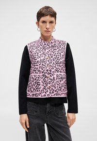 Ροζ γιλέκο με λεοπάρ μοτίβο, με ψηλό γιακά, μπροστινό κλείσιμο με κουμπιά και δύο τσέπες. Φοριέται πάνω από ένα μαύρο πουκάμισο με μακρύ μανίκι και άνετη εφαρμογή.