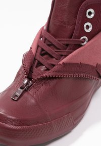 Sneaker alte bordeaux con finitura in pelle, dotate di chiusura con zip, punta testurizzata e dettagli in tessuto a contrasto.