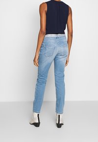Jeans in denim azzurro chiaro con taglio dritto, caratterizzati da una vita stampata, tasche posteriori e dettagli consumati. Abbinati a stivaletti leggeri.