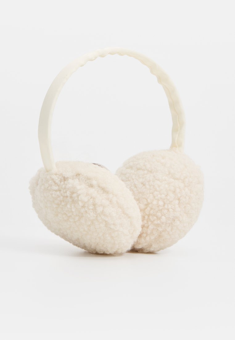 Cremfarbene Ohrenwärmer mit flauschiger, texturiertem Polster und einem glatten, gebogenen Kopfband auf weißem Hintergrund.
