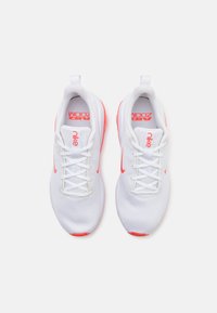 Baskets de sport blanches avec une tige en mesh, accents rose vif et lacets plats. Présente le logo "Nike" sur la languette et sur le côté.