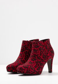 Bottes cheville imprimé léopard rouge et noir avec une texture lisse, un bout arrondi et un talon haut. Dotées d'une fermeture éclair latérale pour un enfilage facile.