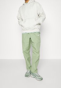 Ljust grå hoodie med geometriskt mönster, kombinerad med ljusgröna cargobyxor med sidofickor och en logotyp. Bärs med gröna sneakers.