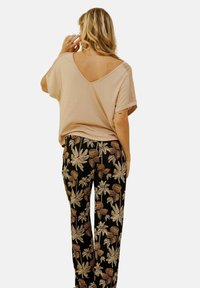 T-shirt beige clair à col V avec des détails en dentelle sur les épaules, associé à un pantalon noir avec un imprimé floral dans des tons crème et doré.
