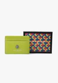 Porte-cartes en cuir vert lime avec quatre fentes, détail de logo métallique, présenté dans une boîte cadeau colorée et à motifs.