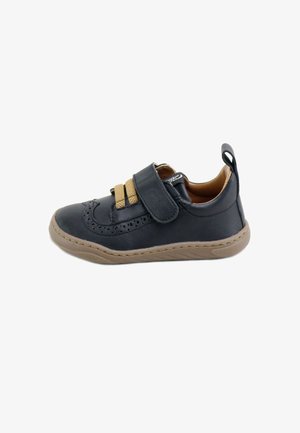 Zapato de cuero negro con acentos marrones, correa de velcro, detalles perforados, punta redondeada y suela de goma texturizada.