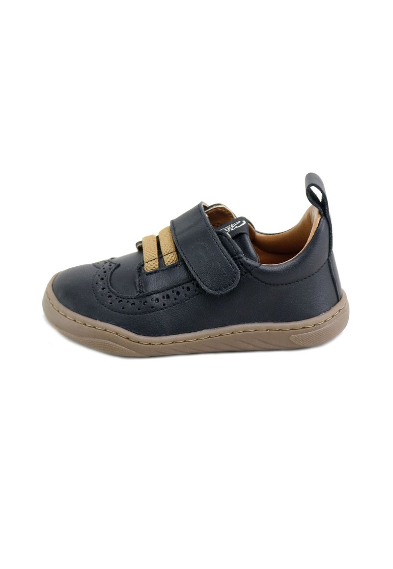 Zapato de cuero negro con acentos marrones, correa de velcro, detalles perforados, punta redondeada y suela de goma texturizada.