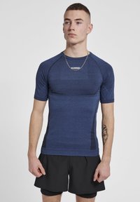 Blå idrottslångärmad skjorta med strukturerad yta, åtsittande design och svarta detaljer på sidorna. Bärs med svarta shorts.